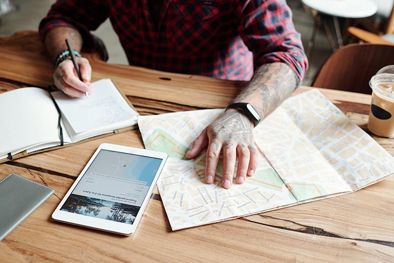 close-up-unrecognizable-tattooed-man-sitting-table-cafe-checking-hotel-location-map-while-planning-trip artist looking for work in the tattoo industry