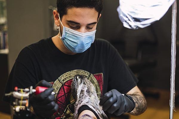 shot-male-tattoo-artist-tattooing-his-client-s-leg apprentice holding a tattoo machine