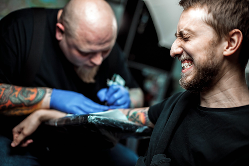 A tattoo client grimacing while being tattooed A tattoo client grimacing while being tattooed
