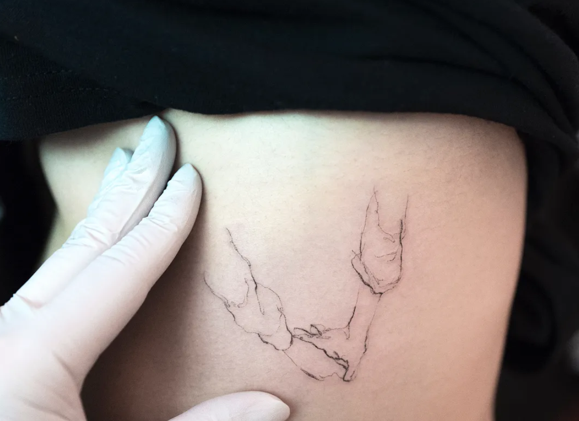 Fine line tattoo of two arms holding hands